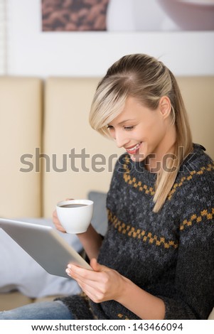 Woman reading an e-book in a restaurant while sitting at a table with a cup of coffee in her hand and the tablet in the other