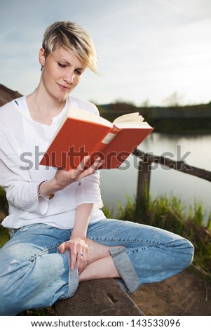 Young beautiful woman reading a book by the country lake