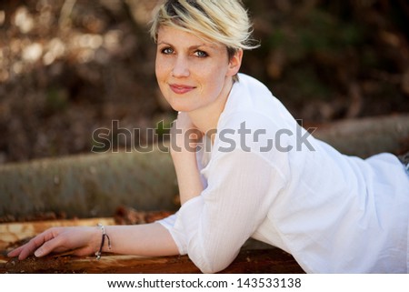 Side Portrait of a beautiful young blond woman lying on logs