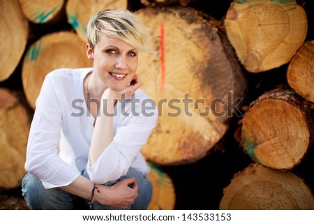 Portrait of a casual blond woman smiling against stack of logs