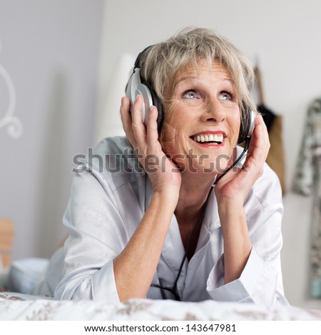 Happy senior woman listening to music through headset while looking up in bed