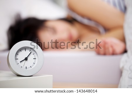 Close up image of alarm clock over the blurred sleeping woman