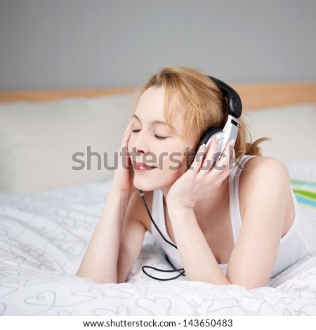 Portrait of a young woman relaxing and listening to music with headphones in her bedroom.