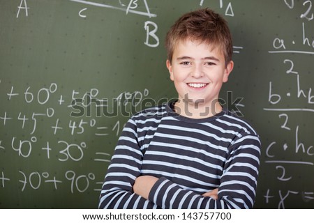 Profile portrait of a smiling schoolboy standing near the blackboard in classroom.