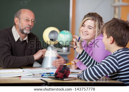 Senior male teacher and students looking at planetarium model at desk in classroom