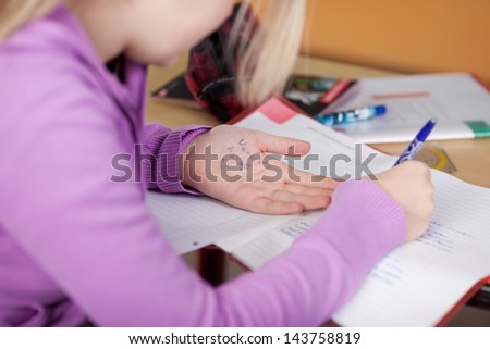 Midsection of female student copying from cheat sheet on hand at desk