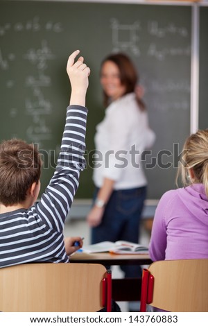 A male student raising his arm to ask a question in the classroom.