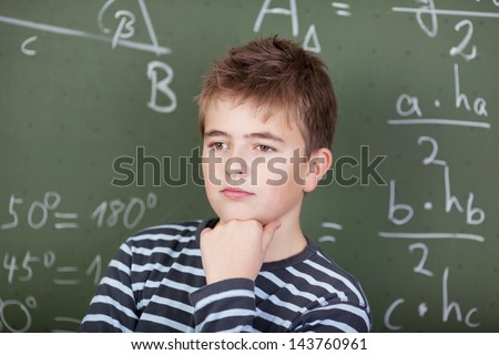 A young schoolboy thinking about something, standing near the blackboard in mathematics class.