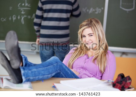 Full length portrait of teenage female student with feet on desk in classroom