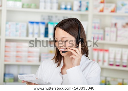 Happy mid adult female pharmacist conversing on headset in pharmacy