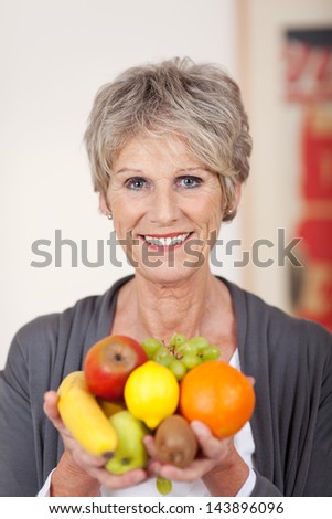 Portrait Of A Smiling Senior Woman Holding A Variety Of Fruits In Her Hands