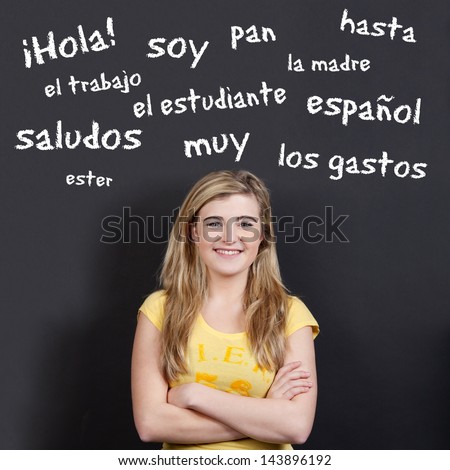 Portrait of a confident smiling teenage girl with arms crossed against Spanish vocabulary on black background