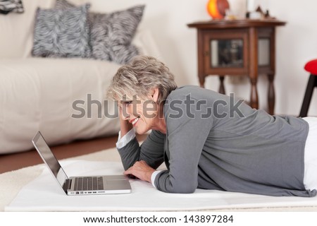 Image Of An Elderly Happy Woman Lying On The Floor And Working On The Laptop.