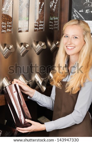 Portrait of happy young waitress filling coffee beans from dispenser at cafe