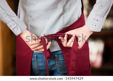 Rear midsection of waitress tying apron in cafe