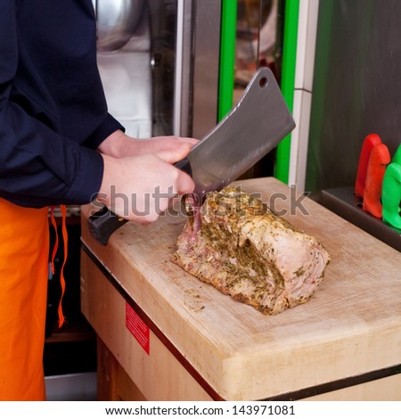 Midsection of butcher cutting meat with cleaver knife on chopping board