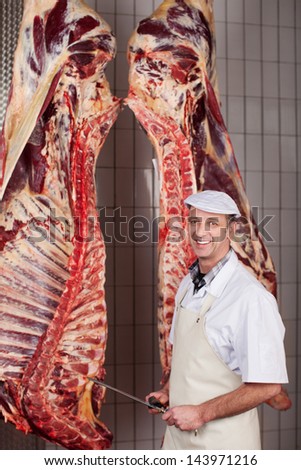 slaughterer sharpening his knife against beef hanging in cold room