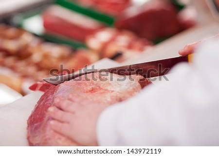 Closeup of butcher\'s hands cutting meat with knife in shop
