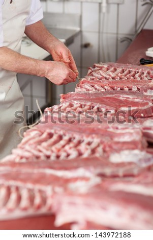 Midsection of male butcher tying rope to meat pieces at counter