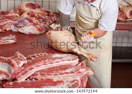 Midsection of male butcher cutting pork meat with knife in shop
