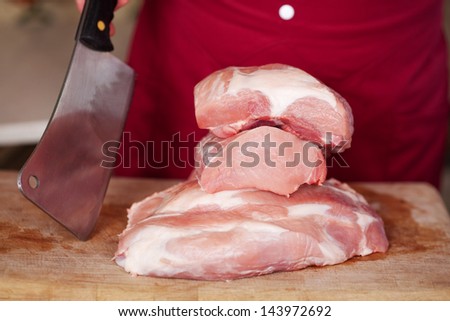 Portions of raw meat piled on a wooden board with a sharp metal cleaver inserted into the wood alongside