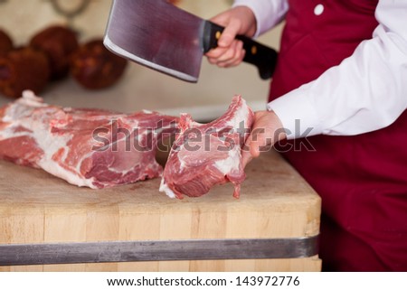 saleswoman with red apron cutting meat with cleaver