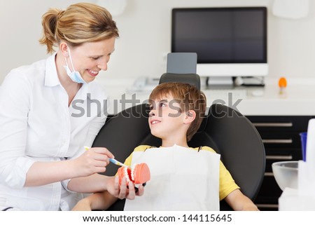 Female dentist explaining brushing procedure to little boy using artificial teeth\'s in clinic