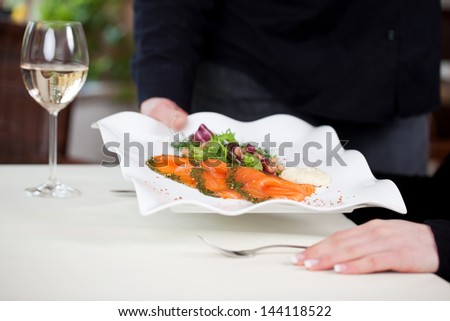 waitress putting salmon dish on table in restaurant