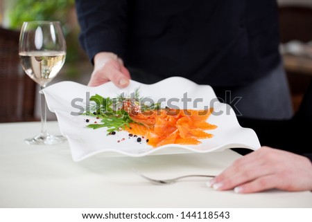 waitress serves sliced salmon dish to female guest