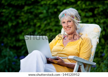 portrait of a smiling elderly lady using laptop in the garden