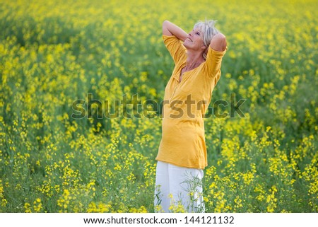 Happy relaxed senior woman with hand behind head standing on field