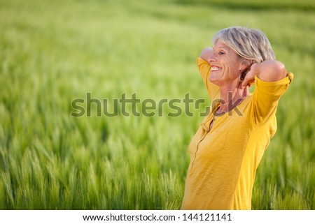 Side view of happy senior woman with hands behind head looking away on grassy field