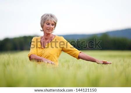 elderly woman walking though field with outstretched arms