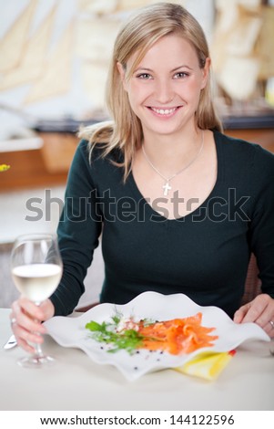 Portrait of happy young woman with white wineglass and food in restaurant