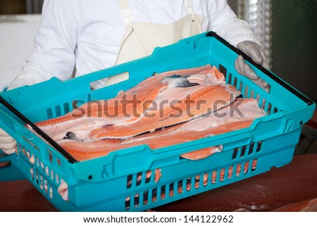 Midsection of worker with sliced fishes in crate
