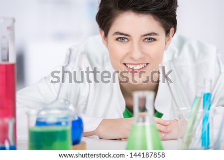 Portrait of confident female scientist with chemicals on foreground in laboratory