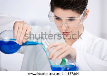 Closeup of beautiful female scientist wearing protective eyewear while mixing chemicals at laboratory