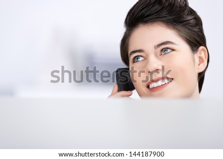 Closeup of young businesswoman looking away while on call in cubicle at office