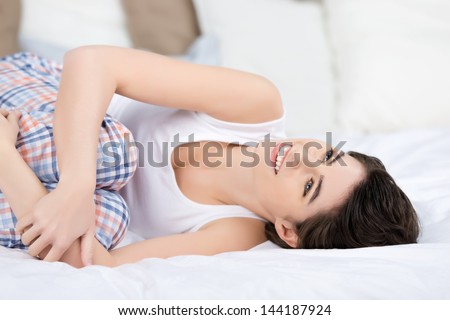 Happy young woman looking away while hugging knees in bed at home
