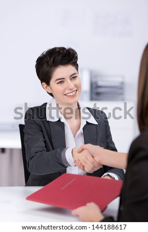 Happy young female candidate shaking hands with businesswoman at desk in office