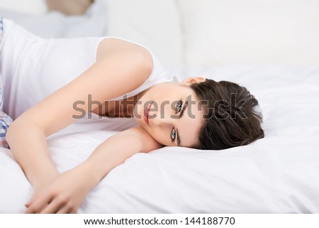 Young lovely female lying on the bed and relaxing in her bedroom.