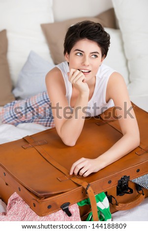 Smiling woman with a packed suitcase lying on her bed in her sleepwear dreaming of her holiday