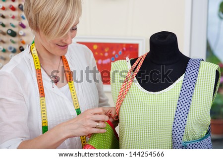 Female fashion designer fixing bag\'s strap on mannequin in workshop