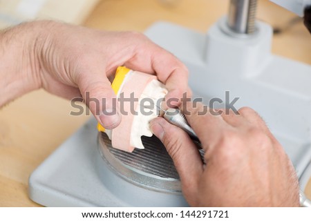 Closeup of dental technician\'s hands shaping artificial teeth with drill in workshop