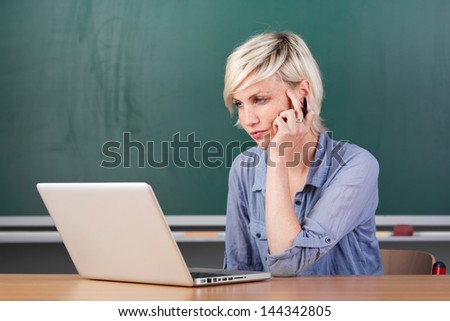 Serious young female teacher using laptop at school table