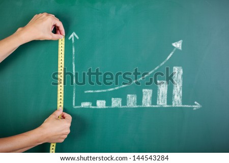 Closeup Of Woman\'S Hands Measuring Bar Graph With Tape On Blackboard