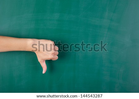 Closeup of woman\'s hand gesturing thumbs down against chalkboard