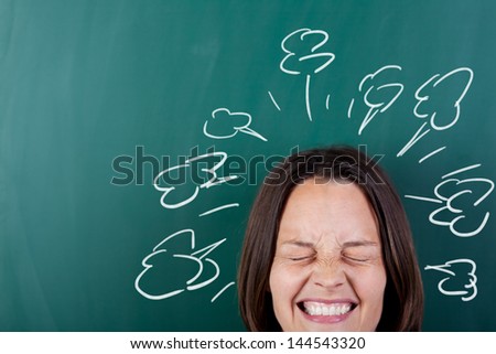 Closeup of angry woman with eyes closed clenching teeth against chalkboard