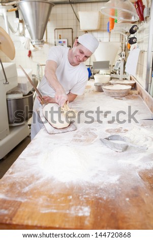 Chef at work in a bakery putting the fial touches to an unbaked loaf of bread before placing it in the oven