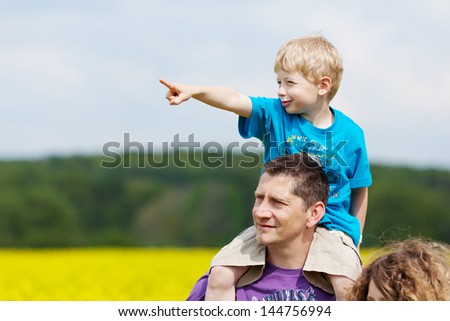 little boy sitting on his fathers shoulders pointing forward
